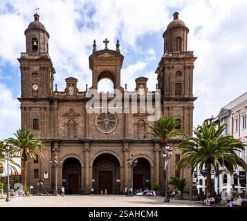 Ein großes historisches Gebäude mit einem großen Uhrenturm und komplexen architektonischen Details, umgeben von Palmen und Menschen auf einem belebten Platz darunter Stockfoto