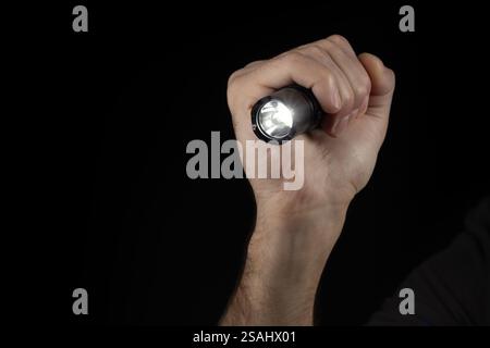 Schwarze Taschenlampe in menschlichen Händen auf schwarzem Hintergrund, einschließlich eines weißen Strahls. Stockfoto