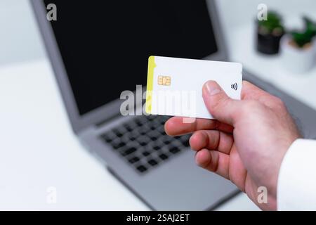 Nahaufnahme einer männlichen Hand, die Kreditkarte vor dem Laptop hält Stockfoto