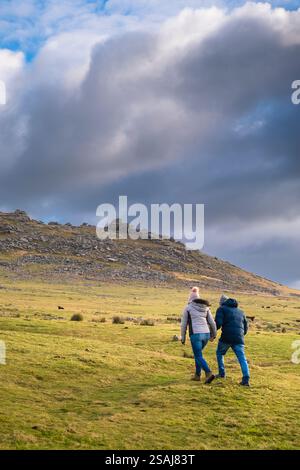 Zwei Personen gehen auf den imposanten Granitgrat Roughtor Rough Tor auf dem wilden windgepeitschten Bodmin Moor in Cornwall in Großbritannien. Stockfoto