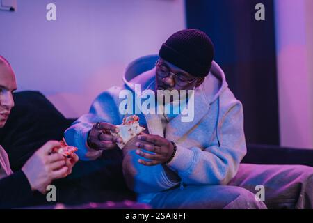 Ein entspannter Moment, in dem zwei Freunde Pizza teilen und einen zwanglosen Abend gemeinsam in einem warmen, beleuchteten Raum genießen. Stockfoto