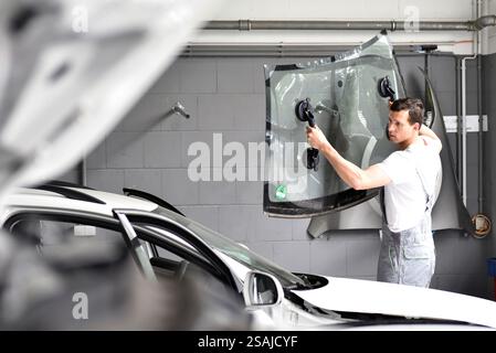 Mechaniker in der Garage ersetzt defekte Windschutzscheibe eines Autos Stockfoto