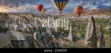 Heißluftballons fliegen Touristen über die spektakulären weltberühmten Felsformationen des „Love Valley“ bei Sonnenaufgang, in der Nähe von Goreme, Kappadokien, Türkei. Stockfoto