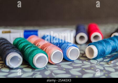 Rollen aus verschiedenfarbigem Garn auf grünem floralem Hintergrund Stockfoto