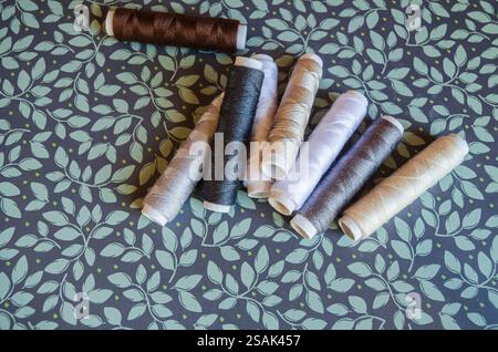 Rollen aus verschiedenfarbigem Garn auf grünem floralem Hintergrund Stockfoto