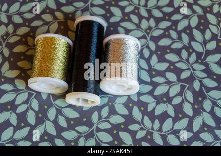 Rollen aus metallischem Garn, Gold, Silber und Schwarz auf grünem floralem Hintergrund Stockfoto