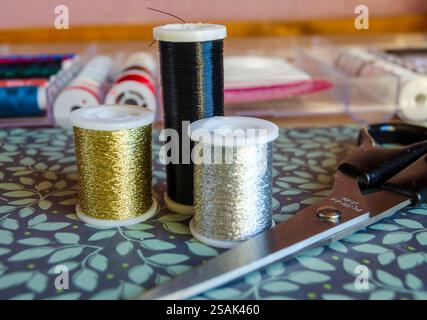 Rollen aus metallischem Garn, Gold, Silber und Schwarz auf grünem floralem Hintergrund mit Schere Stockfoto