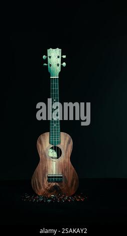 Ukulele, helle Malerei im Dunkeln, brauner Hintergrund, schwarzer Vordergrund und rote Glasperlen. 2025 Stockfoto