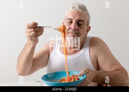 Ein typischer süditalienischer Mann aus Apulien, von vorne gesehen, der einen Teller Spaghetti mit Tomatensauce hält. Er hebt seine Gabel mit der Nudelrolle Stockfoto