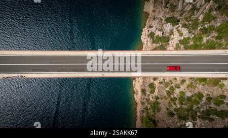 Blick von oben nach unten auf ein rotes Auto allein, das auf einer Brücke über das Meer fährt. Hintergrundbilder für Reisen, Urlaub, die Schönheit des Autofahrens Stockfoto