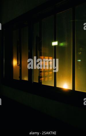 Abstrakte Nachtaufnahme von beleuchteten Glasfenstern mit Reflexionen von Neonlichtern. Der Kontrast zwischen warmen und kühlen Tönen sorgt für ein Kino und Mys Stockfoto