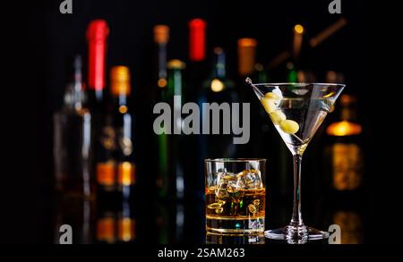 Martini Cocktail und Whiskey auf den Felsen auf einem Bartisch. Das farbenfrohe Bokeh der beleuchteten Flaschen im Hintergrund verbessert die Stimmung und sorgt für einen Dye Stockfoto
