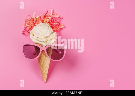 Ein verspielter Eisbecher mit stylischer Sonnenbrille vor einem leuchtend rosa Hintergrund, der Sommeratmosphäre und Spaß verströmt Stockfoto