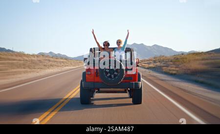 Freunde Auf Roadtrip, Die Ein Cabriolet Auf Der Landstraße Fahren, Mit Frauen, Die Hinten Winken Stockfoto