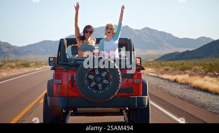 Freunde Auf Roadtrip, Die Ein Cabriolet Auf Der Landstraße Fahren, Mit Frauen, Die Hinten Winken Stockfoto