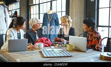 Vier Weibliche Modedesignerinnen Treffen Sich Im Studio, Um Stoffmuster Zu Diskutieren Stockfoto