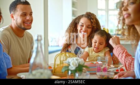 Nahaufnahme Einer Gruppe Von Freunden, Die Sich Der Familie Anschließen, Die Zu Hause Am Tisch Sitzt Und Gemeinsam Das Essen Genießt Stockfoto