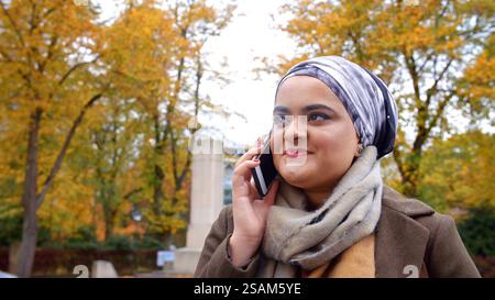 Nahaufnahme Einer Britischen Muslimin, Die Im Autumn Park Auf Dem Handy Spricht Stockfoto