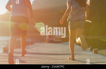 Rückansicht Der Familie, Die Spaß Mit Fischernetzen Auf Dem Holzsteg Am See Bei Sonnenuntergang Mit Lens Flare Hat Stockfoto