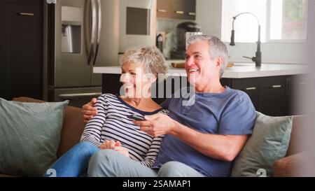 Seniorenpaar sitzen zu Hause entspannt auf dem Sofa und schauen sich eine Show oder einen Film im Fernsehen an Stockfoto
