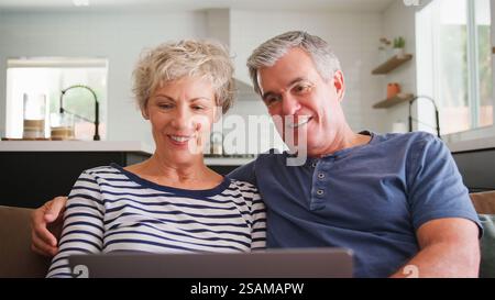 Seniorenpaar Auf Sofa Zu Hause Mit Laptop-Browsing Online-Streaming-Show Oder Abfragen Von Nachrichten Stockfoto