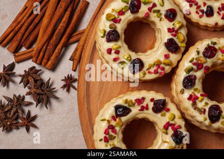 Weihnachtskränzkekse mit getrockneten Beeren und Pistazien auf einem Holzbrett, Blick von oben. Die Komposition vermittelt Feiertagsstimmung, ein Gefühl der Gemeinschaft, A Stockfoto