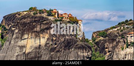Ein Panoramablick auf eine felsige Klippe mit einem historischen Kloster auf der Spitze, umgeben von üppigem Grün und einem klaren blauen Himmel. Die dramatische Landschaft s Stockfoto