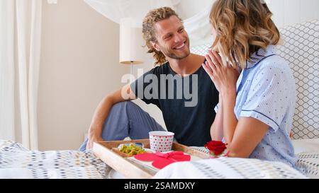 Ein Paar Mit Einem Mann, Der Das Frühstück Der Frau Im Bett Zur Feier Des Geburtstags Oder Des Valentinstages Bringt Stockfoto