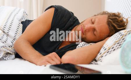 Junger Mann Zu Hause Schläft Im Bett Mit Handy Auf Nachttisch Stockfoto