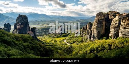 Ein Panoramablick auf Meteora, Griechenland, mit hoch aufragenden Felsformationen, umgeben von üppigem Grün und fernen Bergen unter einem teilweise bewölkten Himmel. Stockfoto