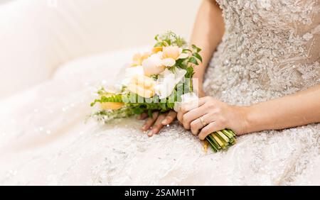 Die Frau trägt ein Hochzeitskleid und hält einen Blumenstrauß. Sie sitzt auf einer Couch Stockfoto