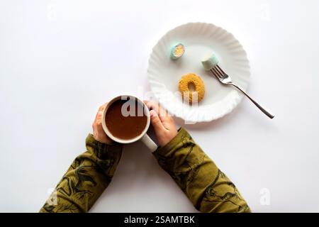 Die Hände eines Kindes halten einen Becher heiße Schokolade und Süßigkeiten in der Nähe, was eine gemütliche und fröhliche Atmosphäre schafft. Stockfoto