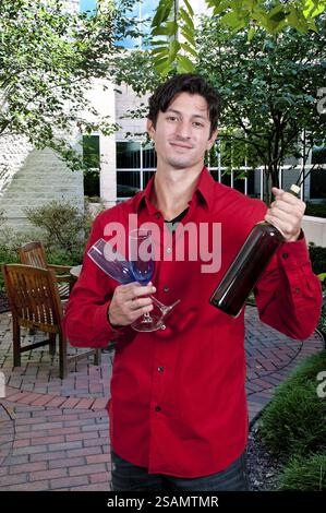Schöner junger Mann, der ein Weinglas und eine Weinflasche hält Stockfoto