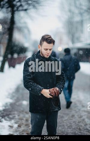 Mann, der auf einer verschneiten Straße steht und einen dunklen Mantel und Handschuhe trägt Stockfoto