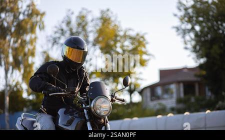 Ein Motorradfahrer fährt bei Tageslicht in der Nähe von Häusern und Bäumen Stockfoto