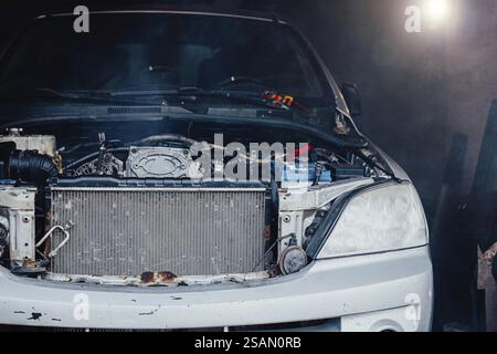 Nahaufnahme des Motorraums eines Autos mit sichtbaren Komponenten und einer blauen Batterie bei schwachem Licht Stockfoto