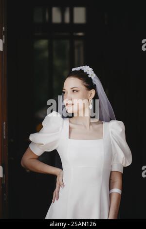 Eine Braut in einem weißen Kleid im Vintage-Stil mit Puffärmeln, trägt einen Schleier und verströmt Eleganz und Gelassenheit im Innenbereich Stockfoto