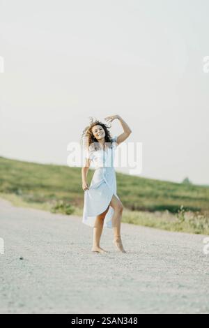 Frau tanzt fröhlich in einem weißen Kleid draußen an einem sonnigen Tag Stockfoto
