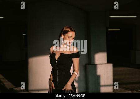 Eine elegant gekleidete Frau in einem schwarzen Kleid posiert nachdenklich in einer sanft beleuchteten urbanen Umgebung Stockfoto