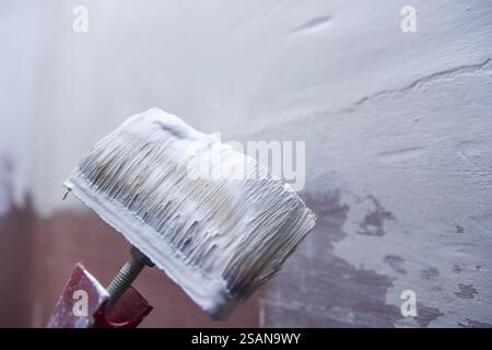 Nahaufnahme eines Pinsels, der weiße Farbe aufträgt und Textur und Pinselstriche an der Wand zeigt Stockfoto