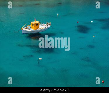 Ankerboot Cherronisos Harbour: Ein kleines Fischerboot im Hafen von Cherronisos, das scheinbar über dem Grund und seinem Schatten durch das kristallklare Wasser aufgehängt ist. Stockfoto