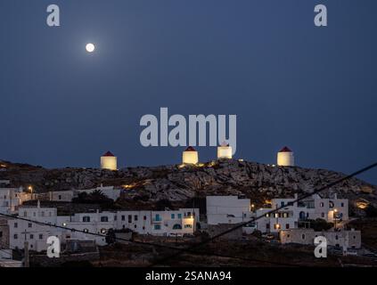 Windmühlen mit Flutlicht und Mondlicht oberhalb von Chora, Amorgos: Vier der Windmühlen von Chora, Amorgos. Leuchten auf einem Kamm über dem Dorf. Ein Vollmond untergeht hinter ihnen. Ihre Flügel und Verkäufe fehlen. Stockfoto