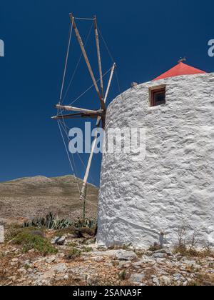 Restaurierte Windmühle aus der Gruppe auf dem Rücken oberhalb des Dorfes Chora: Eine der Windmühlen von Chora, Amorgos, die noch immer ihre Rotorblätter und aufgerollten Segel intakt hat. Eine fischförmige Windfahne oben auf dem orangefarbenen konischen Dach. Stockfoto