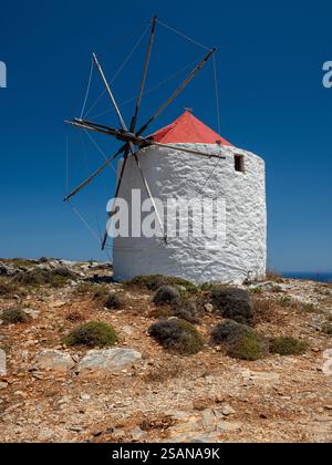 Restaurierte Windmühle aus der Gruppe auf dem Rücken oberhalb des Dorfes Chora: Eine der Windmühlen von Chora, Amorgos, die noch immer ihre Rotorblätter und aufgerollten Segel intakt hat. Eine fischförmige Windfahne oben auf dem orangefarbenen konischen Dach. Stockfoto