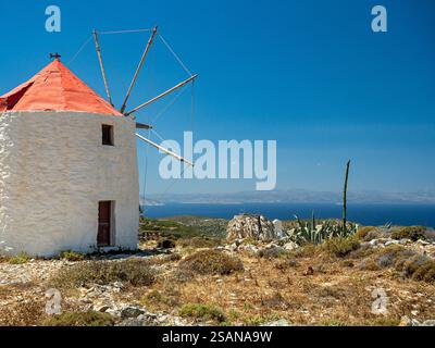 Windmühle, Agean, Keros und Chora Castle: Blaue Ägäis und Insel Keros dahinter. Eine funktionierende Windmühle hoch auf dem Kamm über der Chora und ihrer Burg, deren Gipfel gerade noch hinter dem Kamm zu sehen ist. Stockfoto