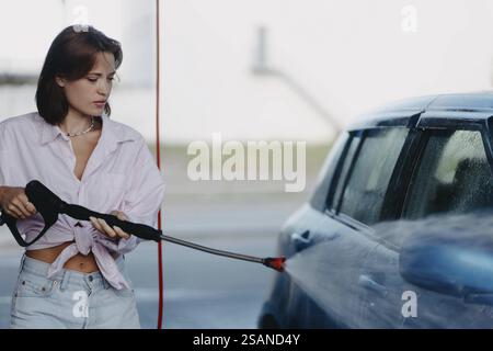 Eine Frau benutzt einen Hochdruckreiniger, um die Seite eines Autos in einer Waschstation zu reinigen Stockfoto