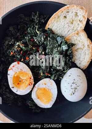 Bratpfanne mit gebratenem Grünkohl mit Gewürzen, gekochten Eiern und Brot. Gesunde Ernährung. Direkt darüber. Stockfoto