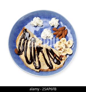 Köstliche Crepes mit Schokoladensauce, Banane, Mandeln und Schlagsahne isoliert auf weiß, Blick von oben Stockfoto