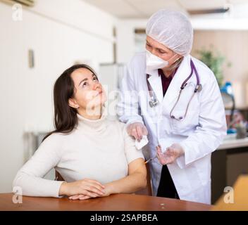 Fokussierte ältere Ärztin, die junge Frau impft Stockfoto