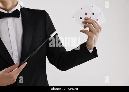 Illusionist zeigt Zauberstab auf Spielkarten vor weißem Hintergrund, Nahaufnahme Stockfoto